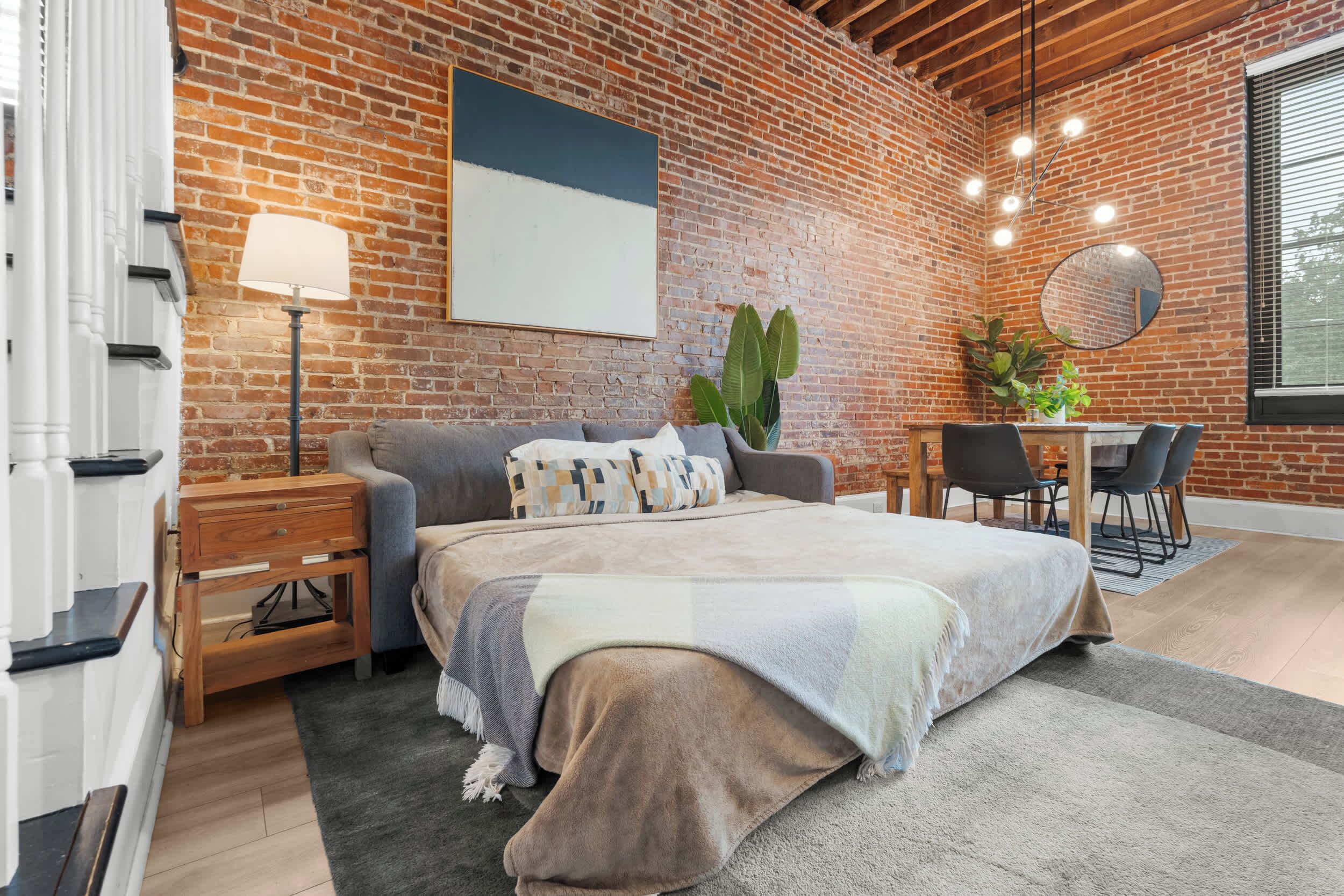 Un dormitorio moderno con pared de ladrillo, una cama grande, un escritorio y una zona de comedor.