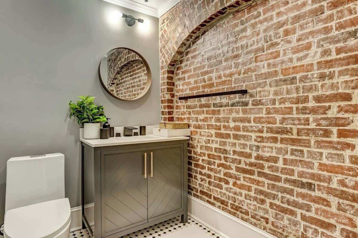 A bathroom with a brick wall, a round mirror, a toilet, and a cabinet.