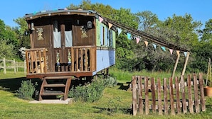 A rustic wooden cabin with a porch, surrounded by a wooden fence and greenery. - Fleur des Champs" caravan, Nordic bath and shared pool (Sigalens)