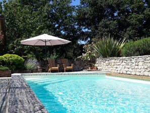 Relax by the serene pool surrounded by lush greenery and a shaded wooden deck.