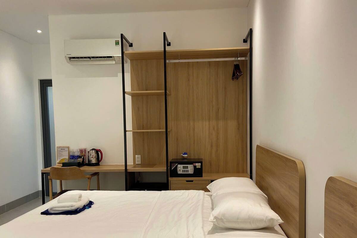 A hotel room with two beds, a desk, a chair, a wardrobe, and an air conditioning unit.