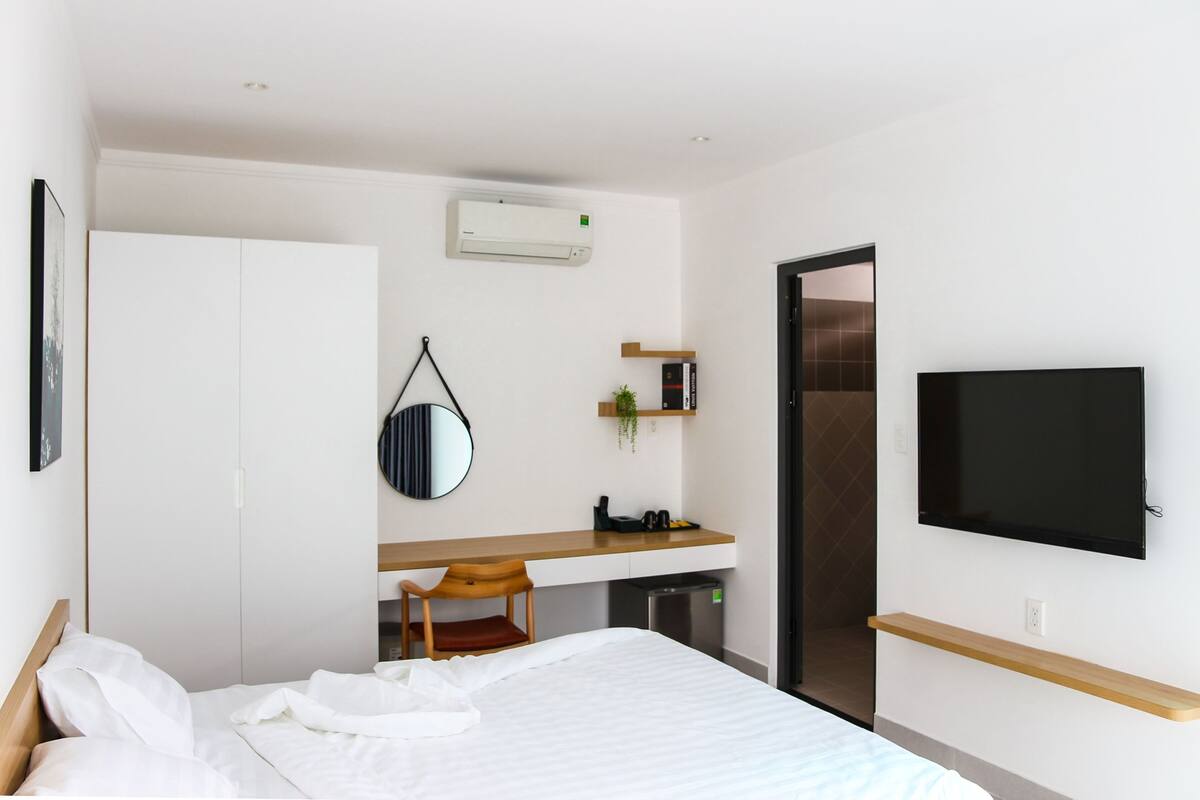 A hotel room with a bed, a desk, a chair, a TV, a wardrobe, and a mirror.