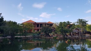 A large building with a red roof and multiple balconies, surrounded by trees and a pond. - Minh Hai Resort (Ho Chi Minh City)