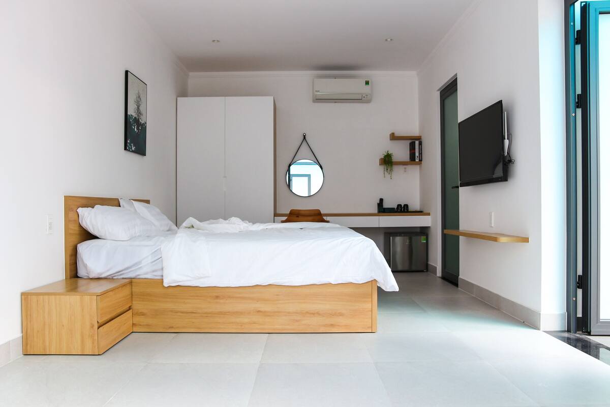 A modern bedroom with a wooden bed, a small desk, a mirror, and a TV.