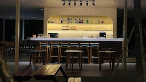 An outdoor bar area with wooden tables and chairs, a counter with a variety of bottles, and string lights overhead. - Minh Hai Resort (Ho Chi Minh City)
