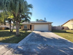 A single-story house with a garage, a front lawn, and a palm tree.