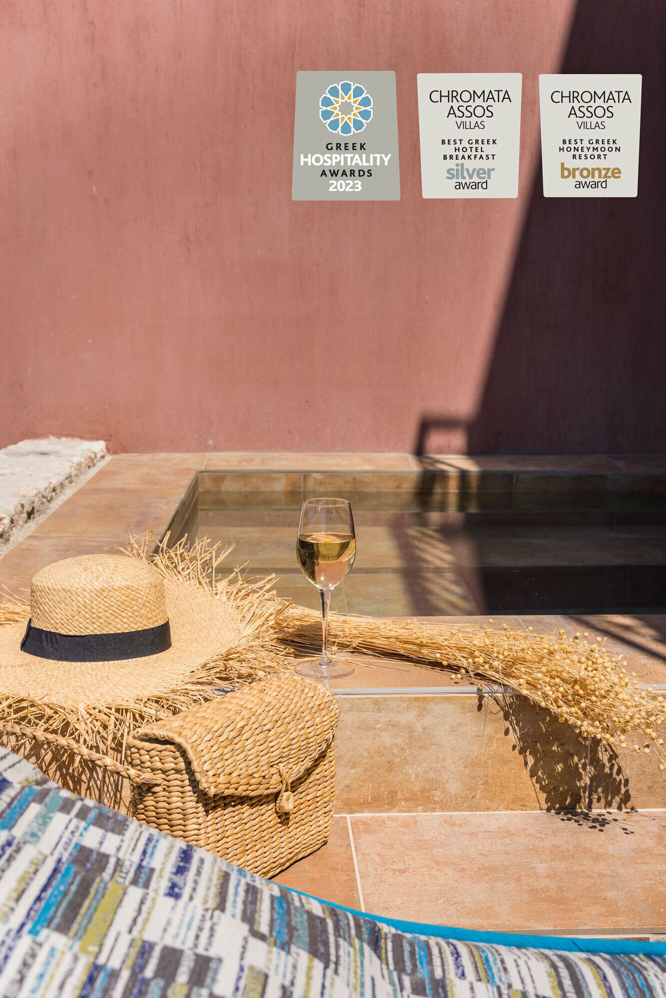 Un espacio al aire libre iluminado por el sol, con un sombrero de paja, una copa de vino blanco y cestas tejidas sobre un suelo de baldosas.