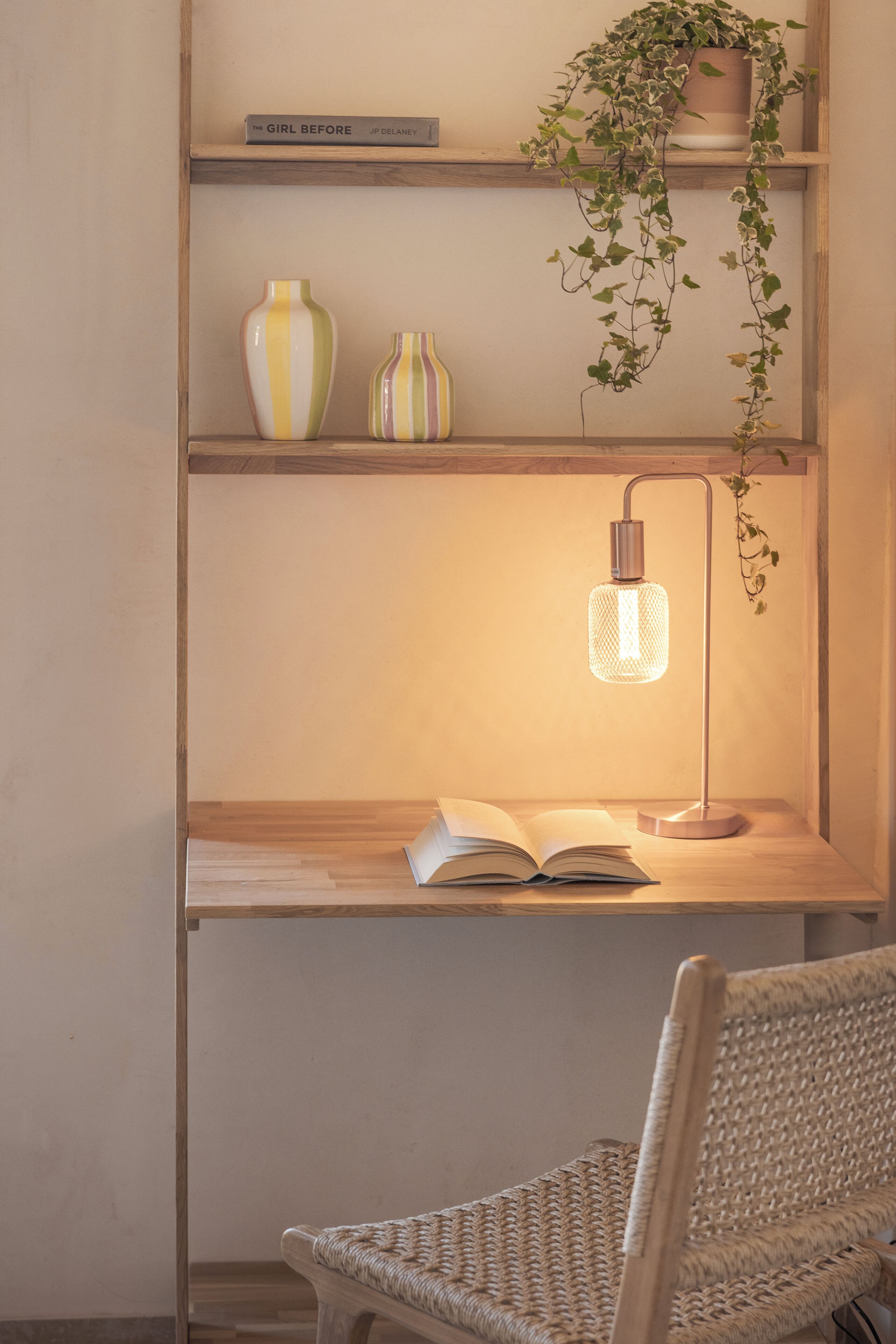 Ein Holztisch mit einem Buch, einer Lampe und einer hängenden Pflanze.