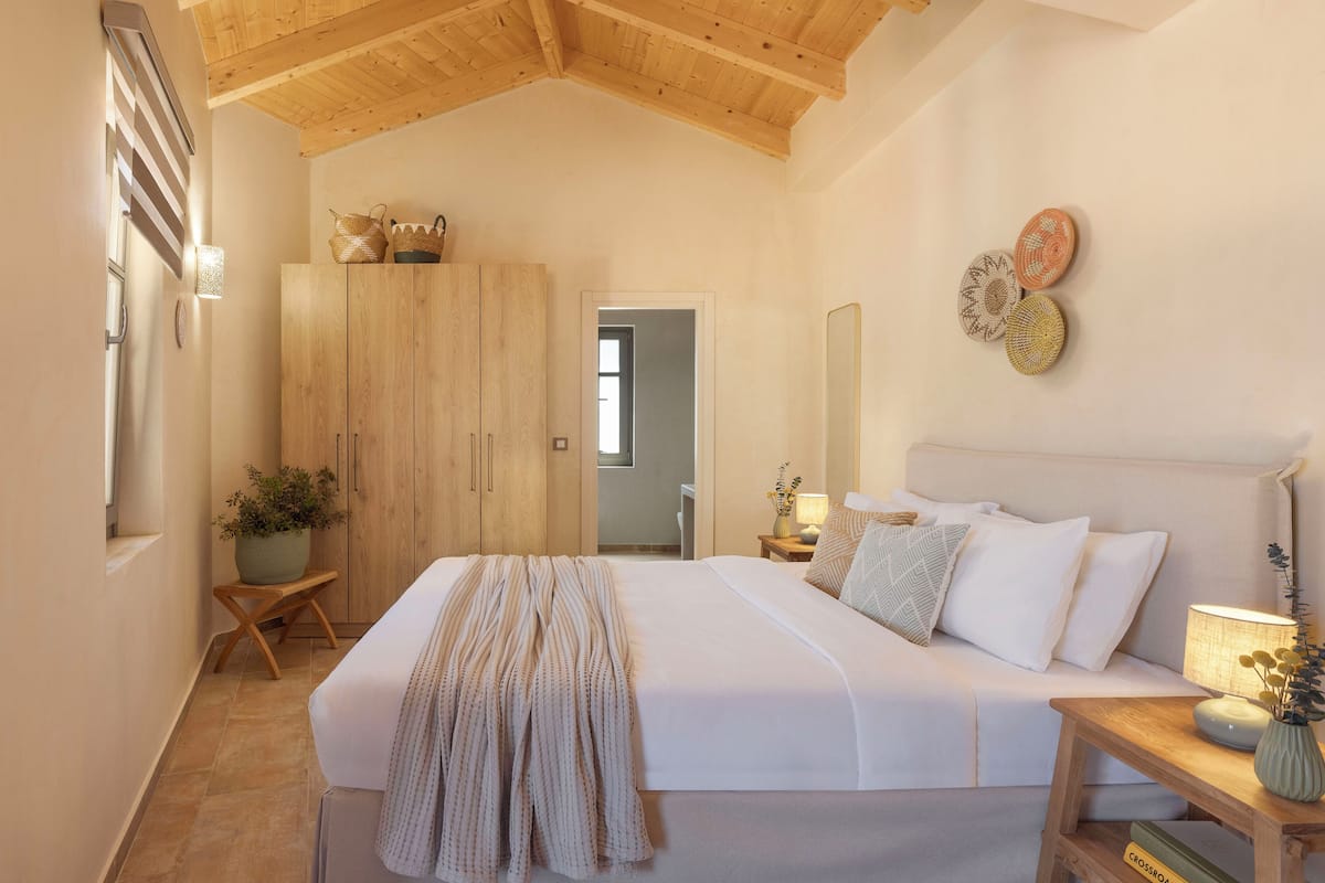 A bedroom with a bed, wooden wardrobe, bedside table, lamp, and wall decor.