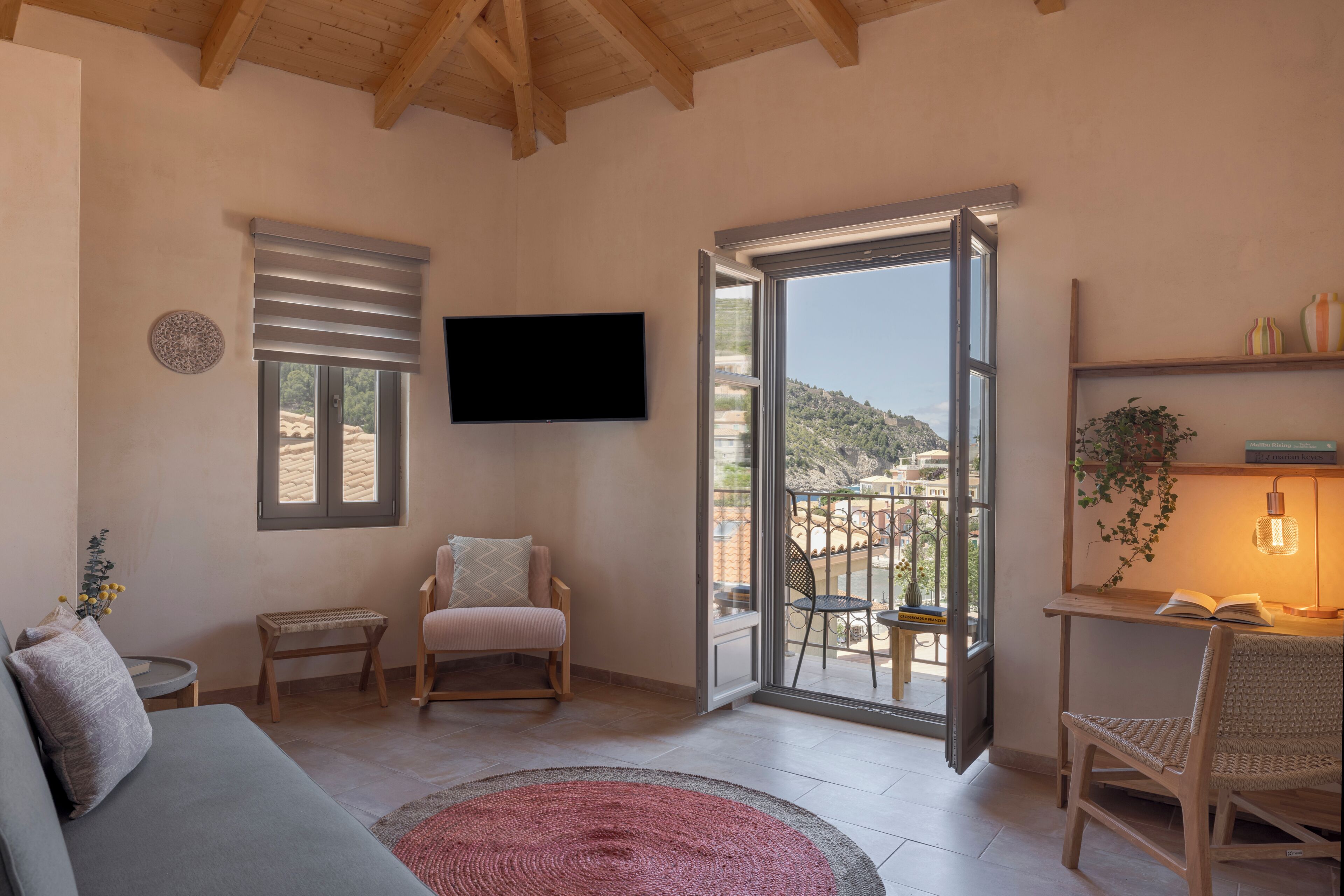 A living room with a sofa, a chair, a small table, a TV, a sliding glass door to a balcony, and a bookshelf.