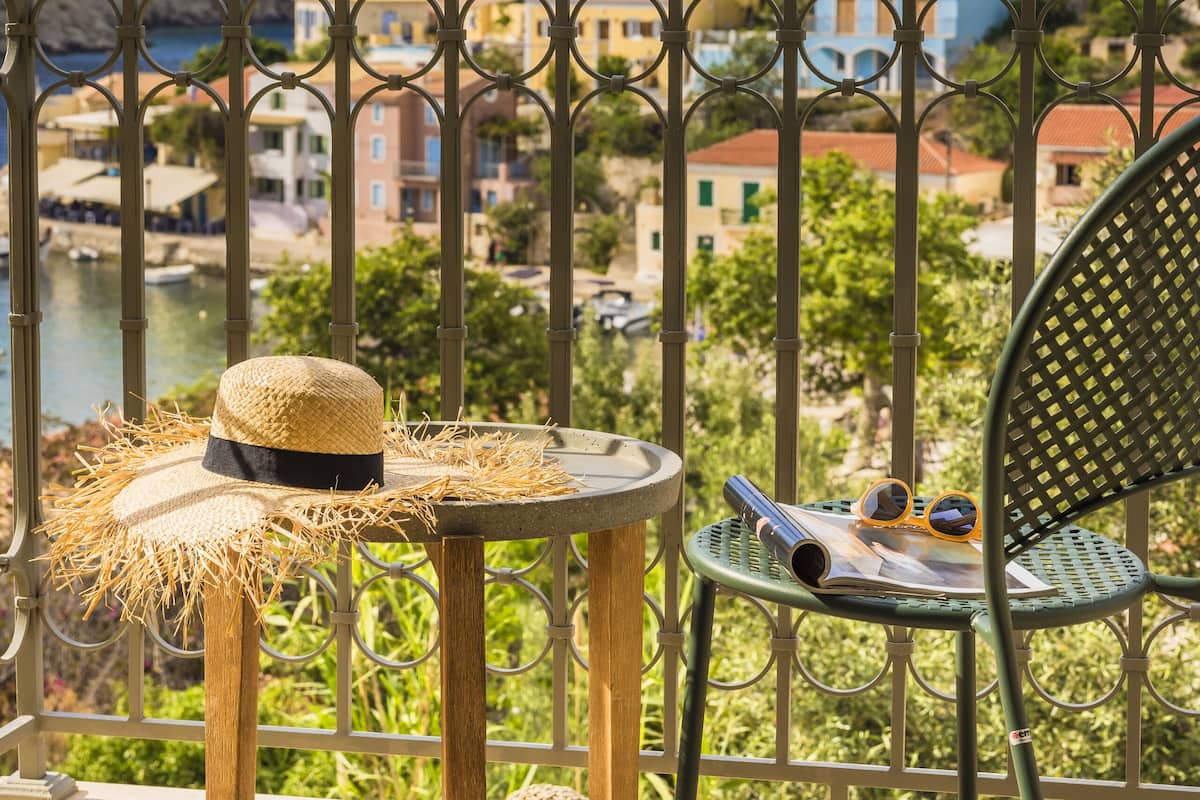 A balcony with a view of a coastal town, a straw hat, and a chair.