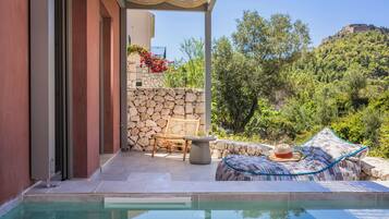 A poolside area with a stone wall, a wooden bench, and a lounge chair with a hat.