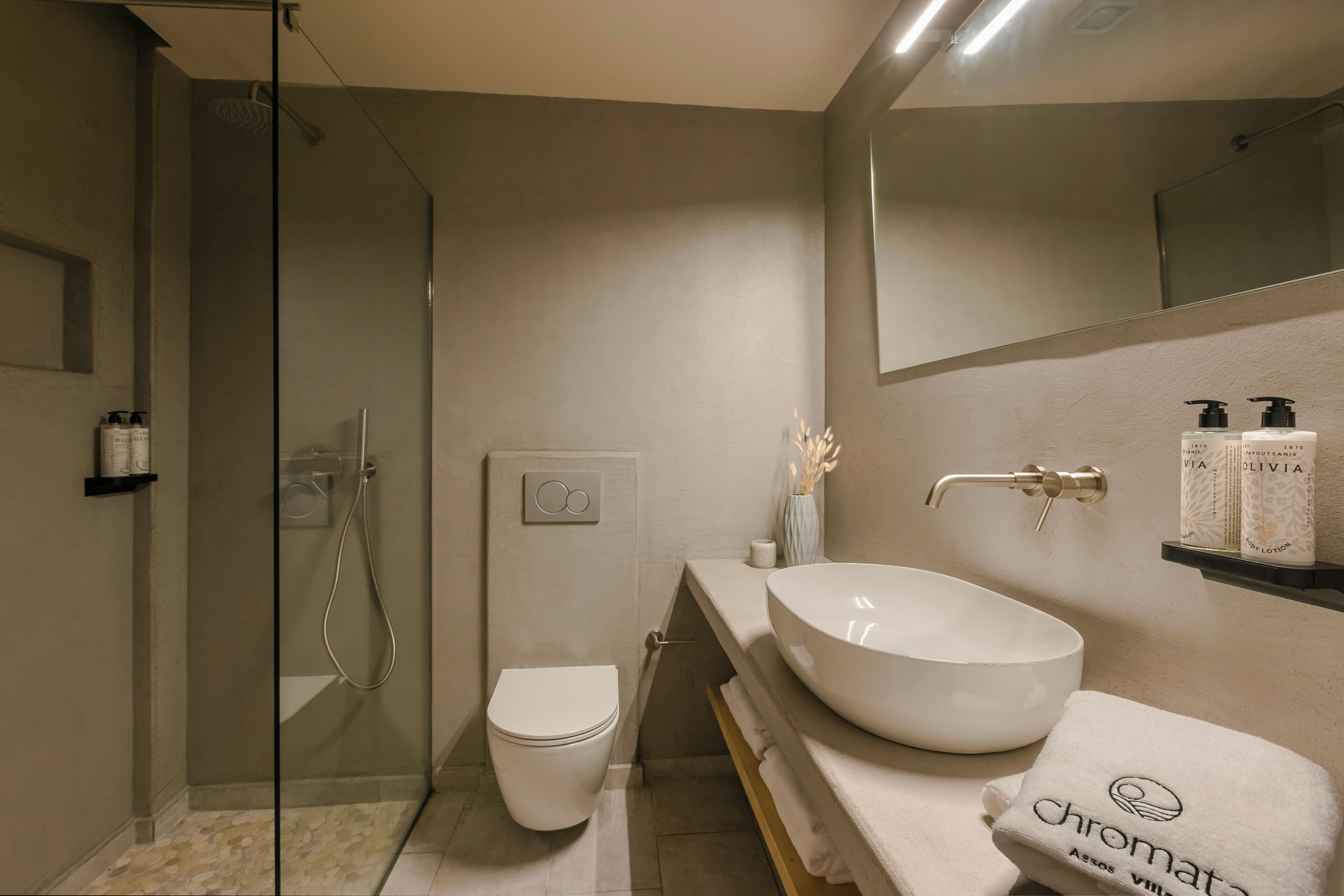 A modern bathroom with a glass-enclosed shower, a toilet, a large vessel sink, and a mirror above the sink.