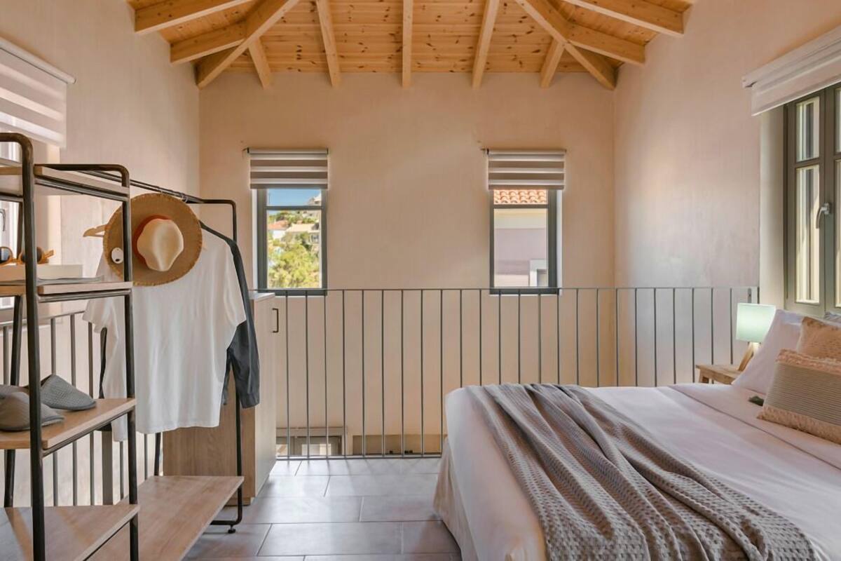 A bedroom with a bed, a wooden bench, a hat on the bench, a window, and a door.