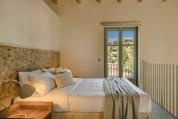 A bedroom with a bed, bedside table, lamp, and a view of a balcony with a door. - Assos Chromata Villas (Kefalonia)