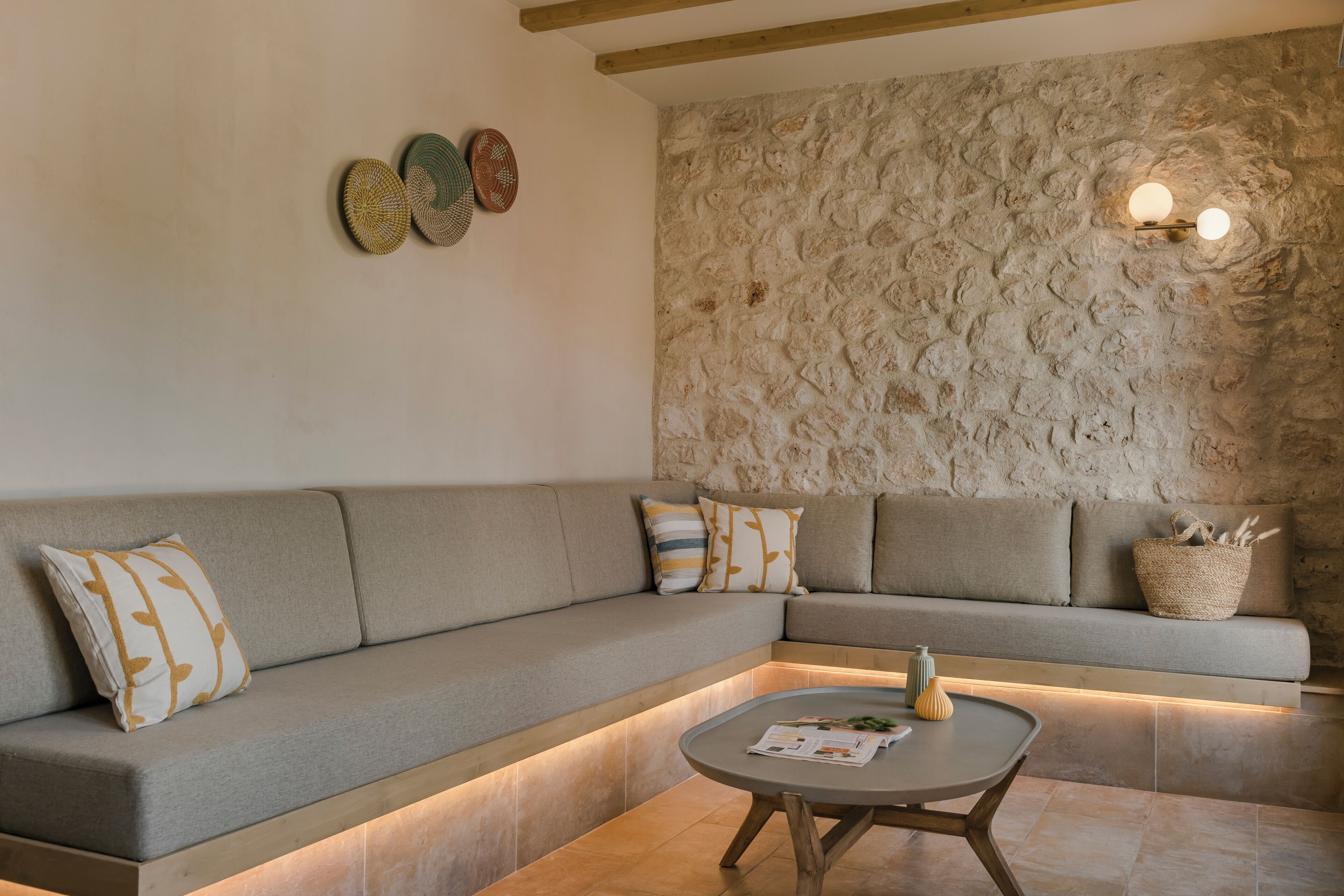 A modern living room with a stone wall, a sofa with cushions, a coffee table, and wall-mounted lights.