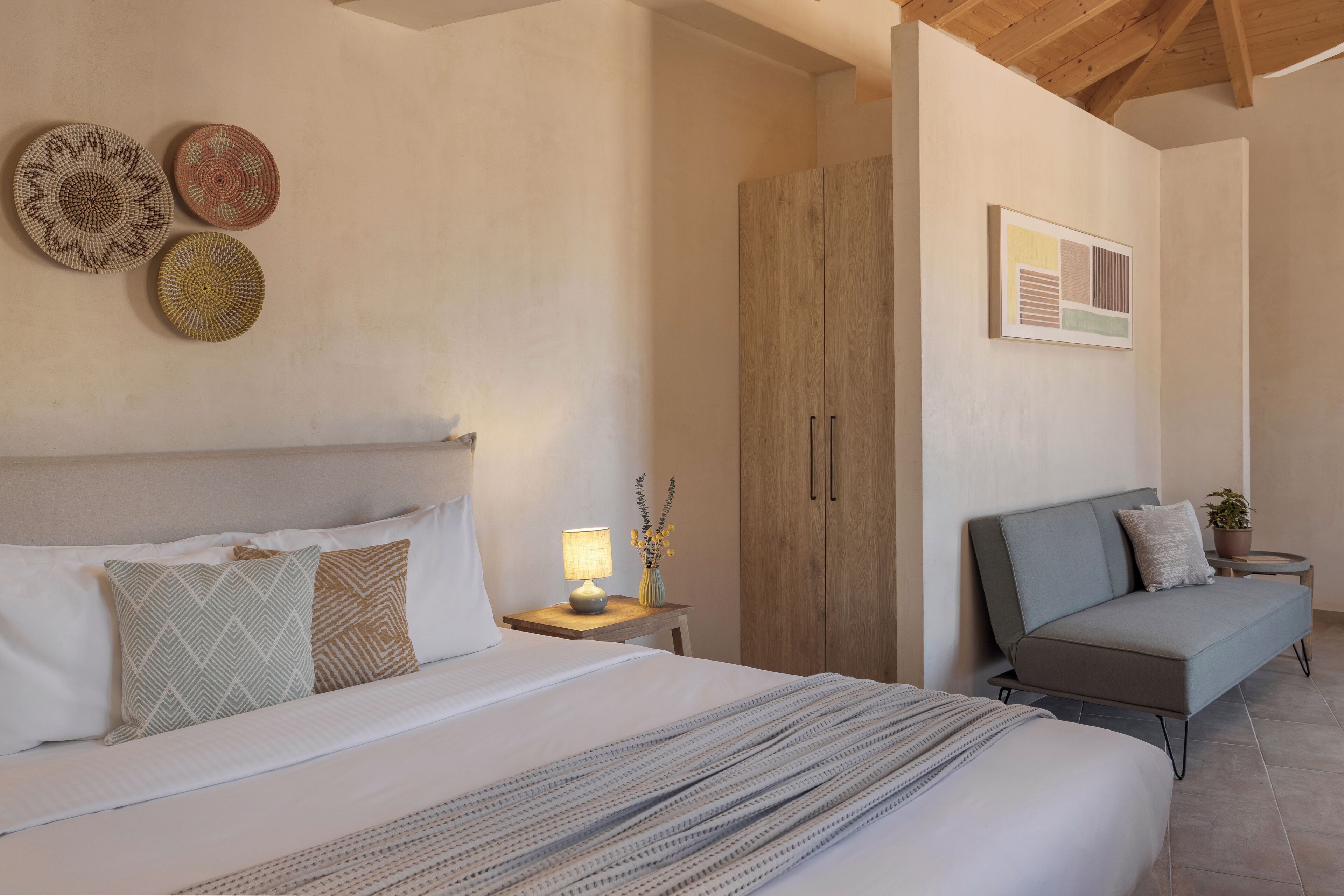 A bedroom with a bed, bedside table, lamp, and a sofa.