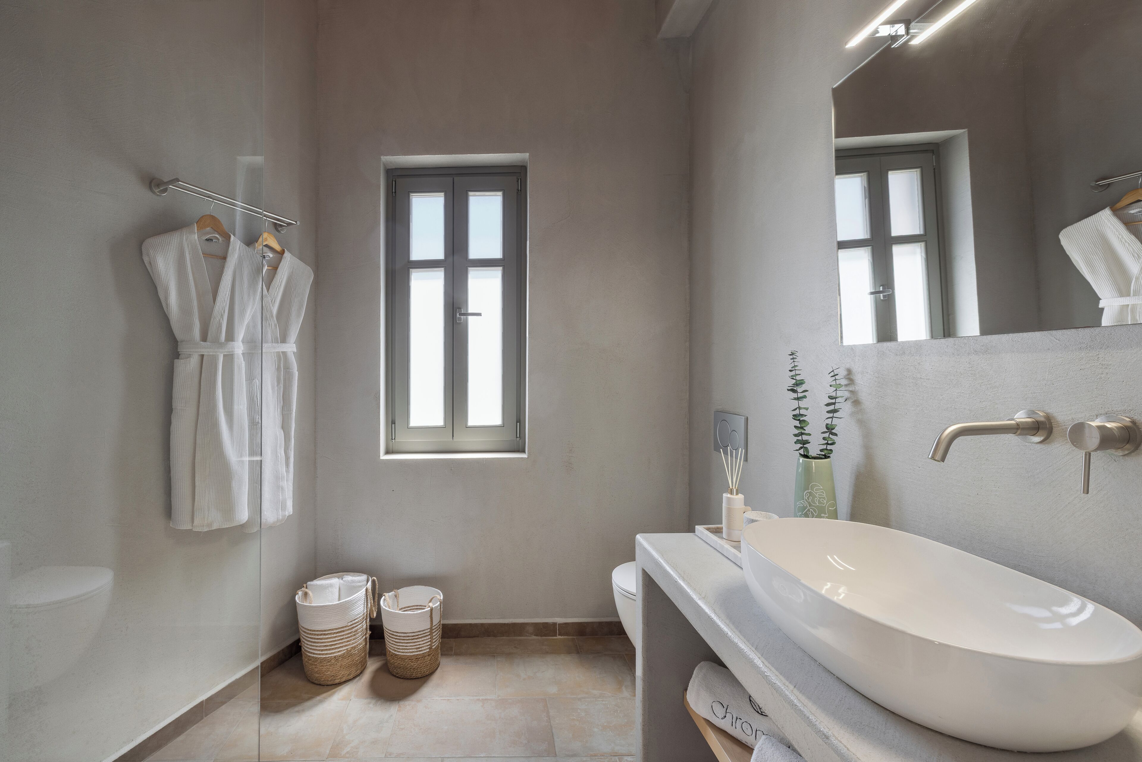 A modern bathroom with a large white sink, a window, and two wicker baskets on the floor.