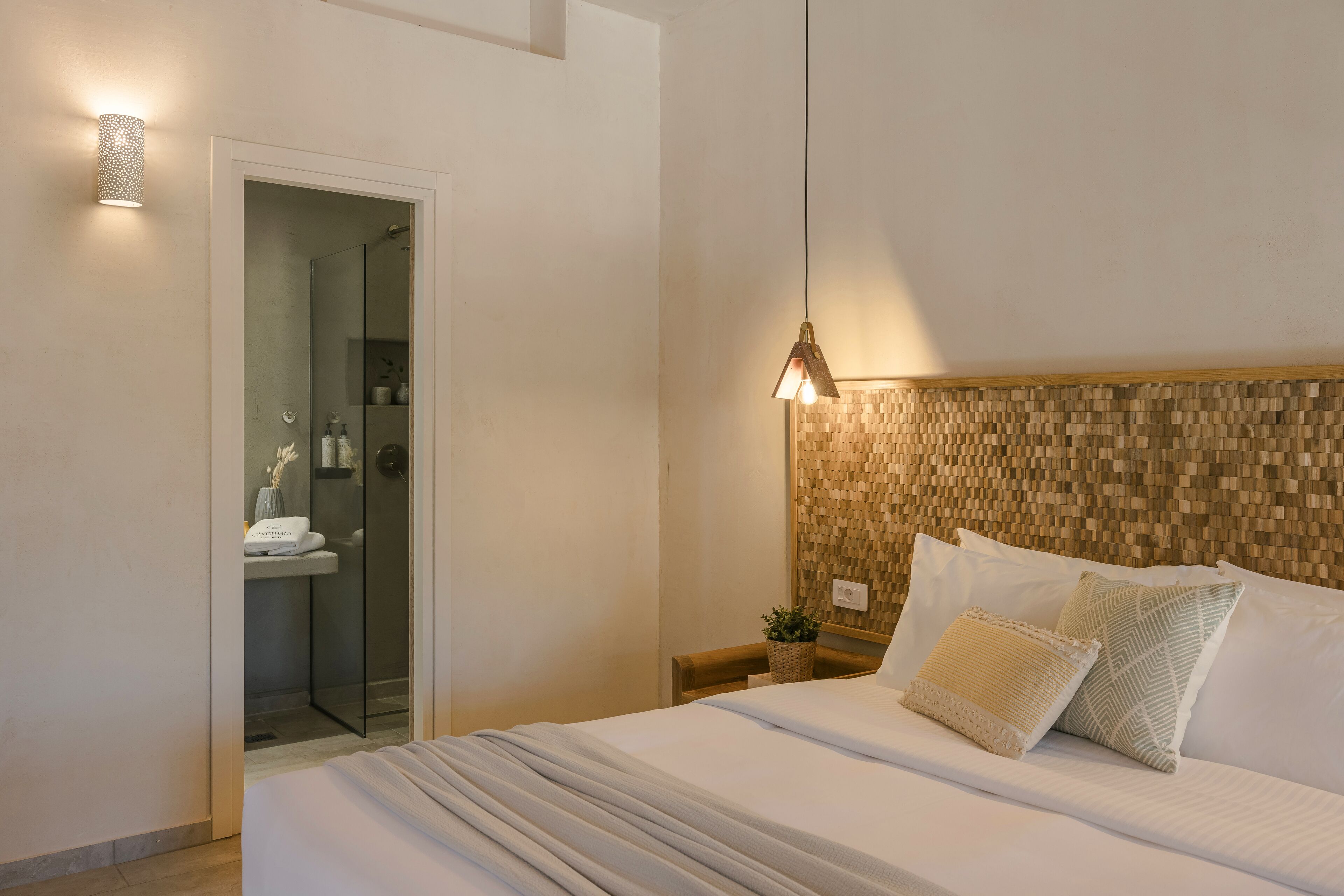 A hotel room with a bed, a nightstand, a wall-mounted lamp, and a shower area.