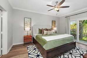 Un dormitorio con cama, mesitas de noche, ventilador de techo y un ventanal con vistas a la vegetación.