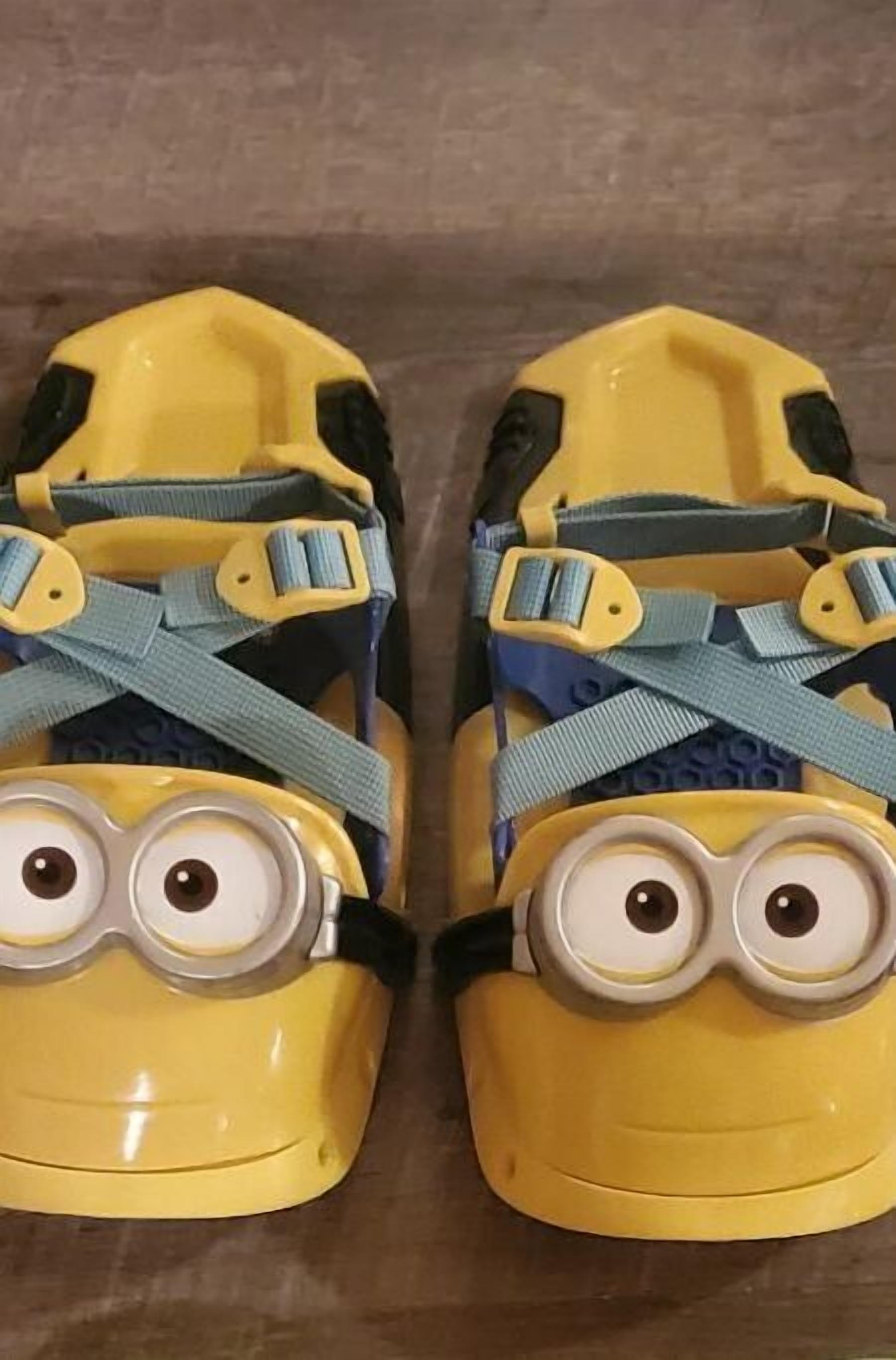 Une paire de chaussures jaunes avec des brides bleues et un motif représentant le visage d’un personnage de « Moi, moche et méchant ».