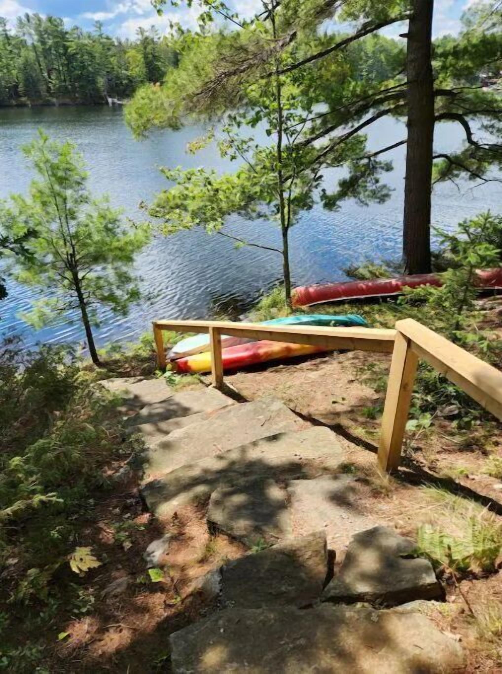 Una terraza de madera con una canoa y un kayak, con vista a un lago rodeado de árboles.
