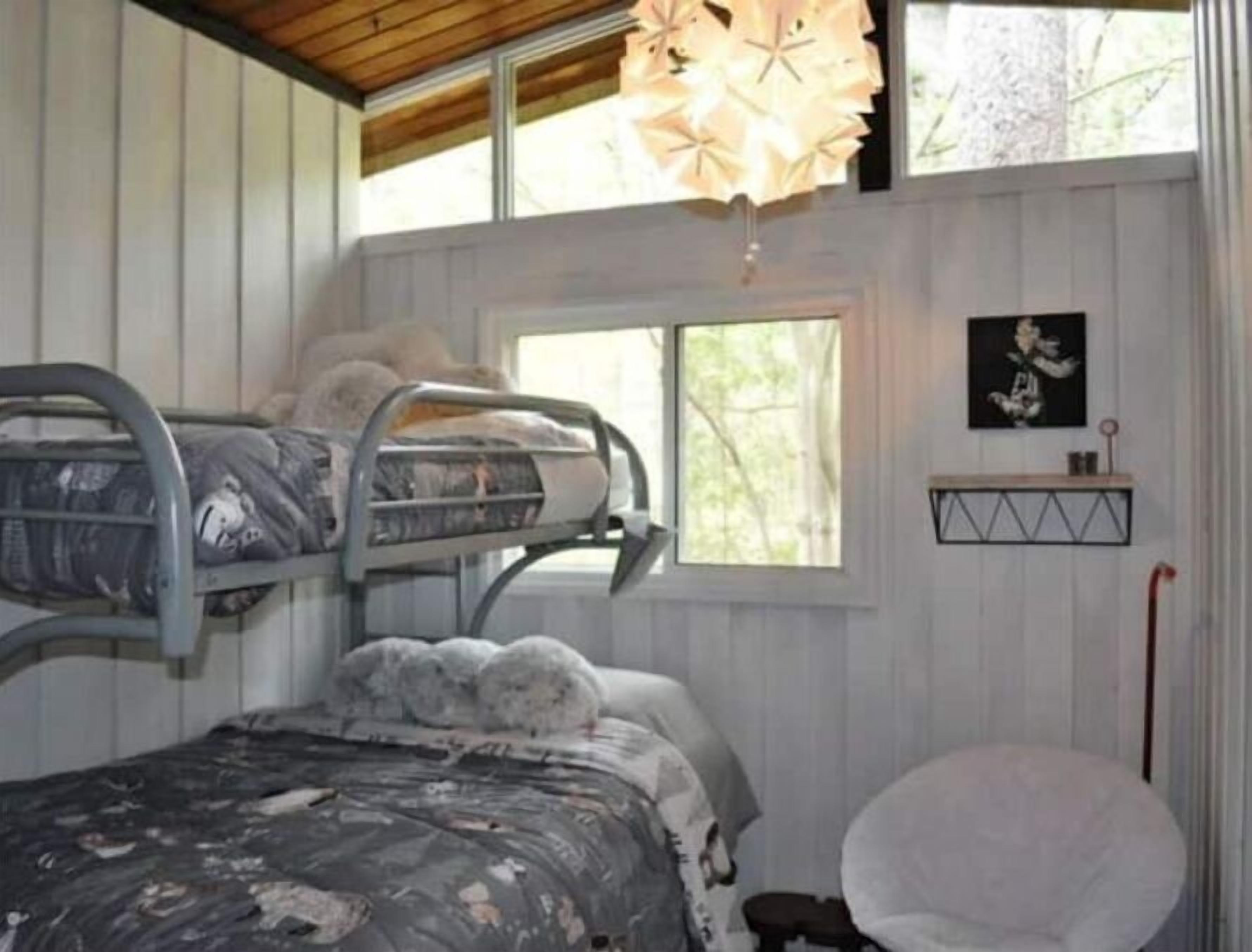 Une chambre avec un lit superposé, une fenêtre, une chaise et une étagère fixée au mur, sur laquelle est posée une image.