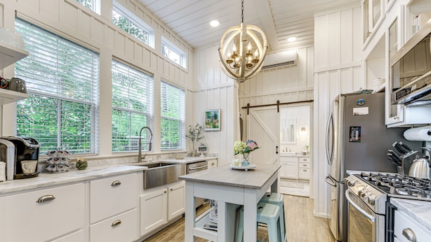 A kitchen with white cabinetry, a central island, stainless steel appliances, and large windows.