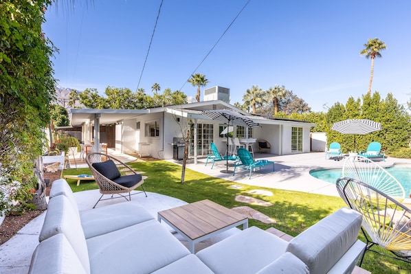 A modern house with a patio, outdoor seating, a pool, and a well-maintained lawn.
