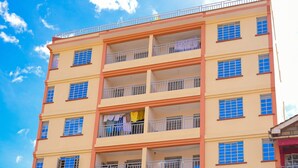 A multi-story building with balconies, a shop on the ground floor, and a red car parked in front. - Classic Beautiful 2-bedroom Apartment in Thika (Thika)