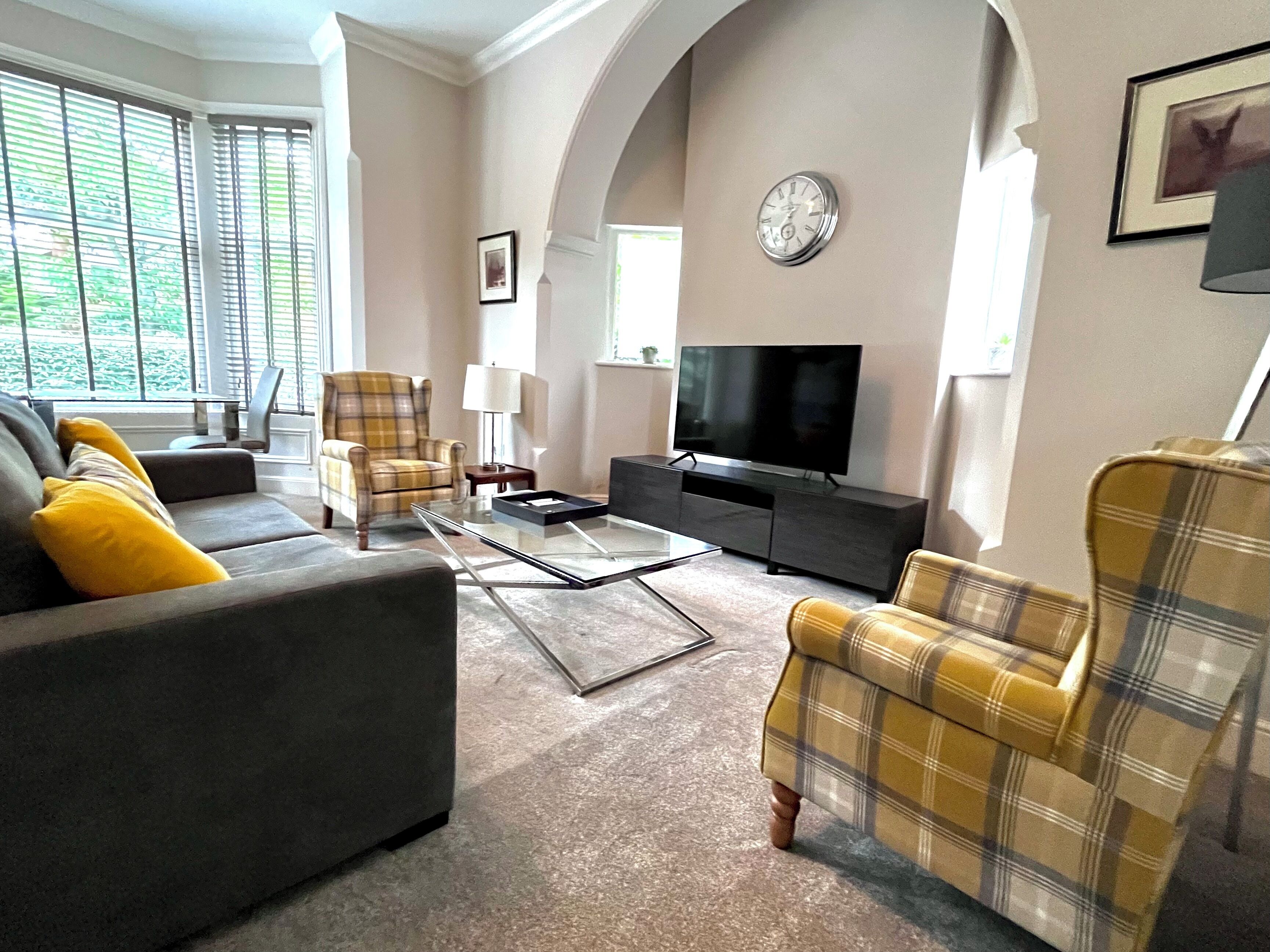 A living room with a sofa, armchairs, a coffee table, a television, and a clock on the wall.