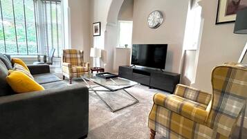 A living room with a sofa, armchairs, a coffee table, a television, and a clock on the wall.