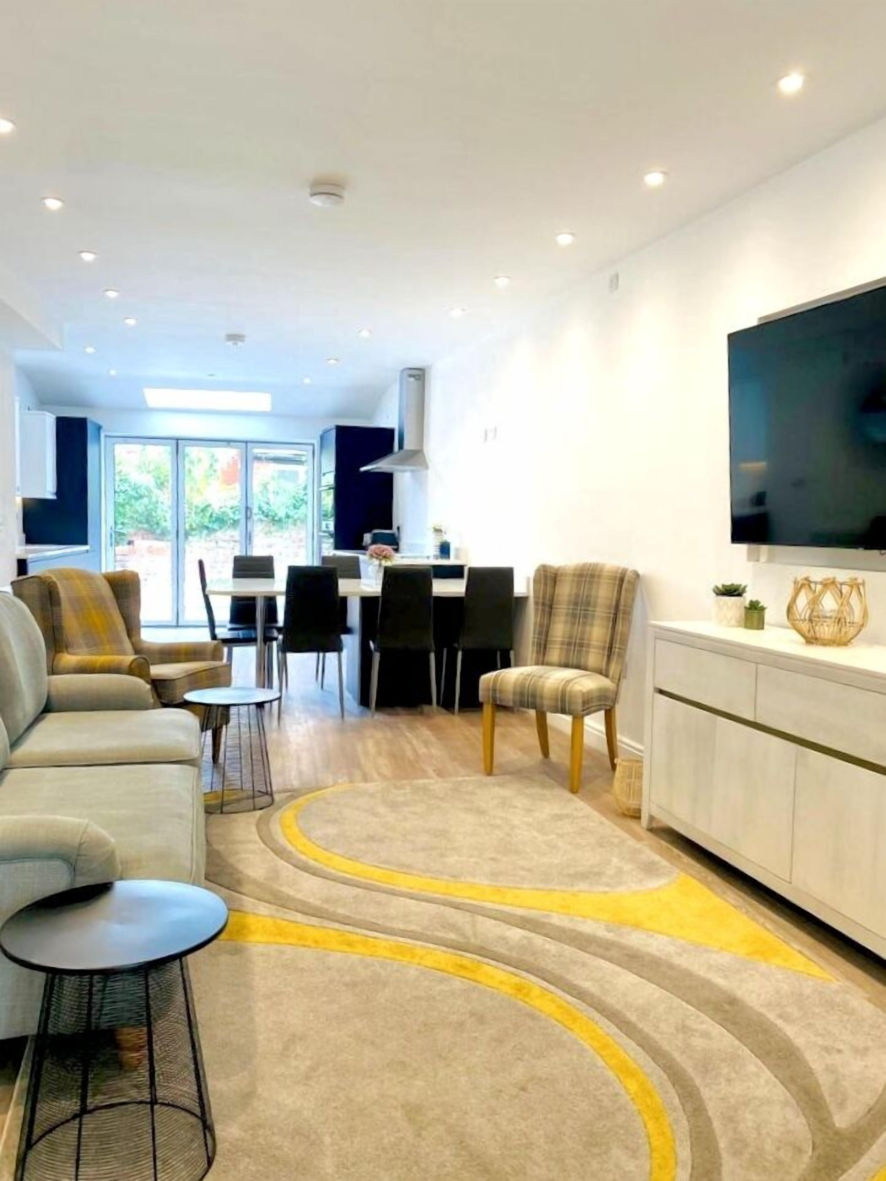 A modern living room with a sofa, chairs, a dining area, and a kitchen in the background.