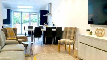 A modern living room with a sofa, chairs, a dining area, and a kitchen in the background.