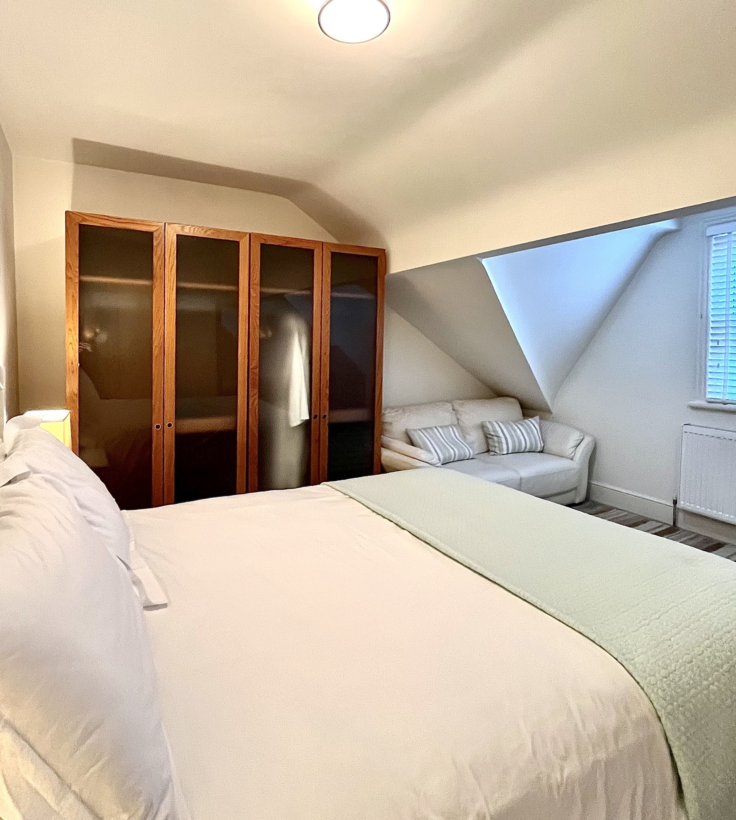 A bedroom with a bed, a wardrobe, a sofa, and a window.