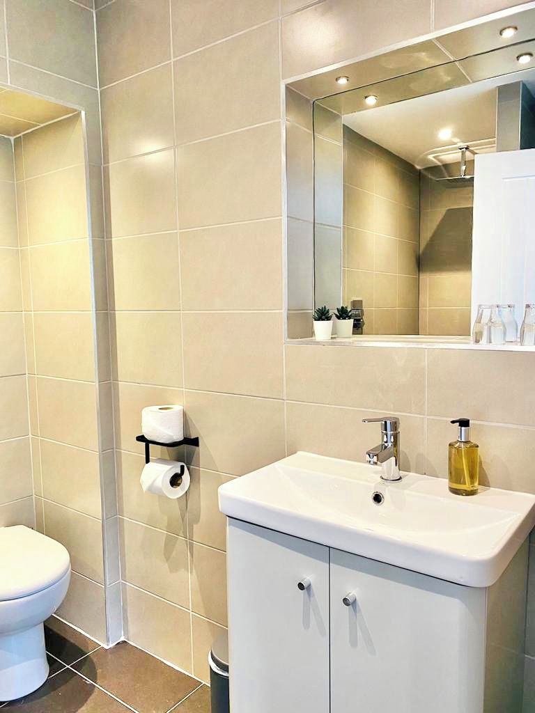 Une salle de bain moderne avec un lavabo blanc, un miroir au-dessus et des toilettes sur la gauche.