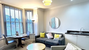 A modern living room with a sofa, a coffee table, and a dining area with a table and chairs. - Mode Apartments St Annes (Lytham St. Anne's)