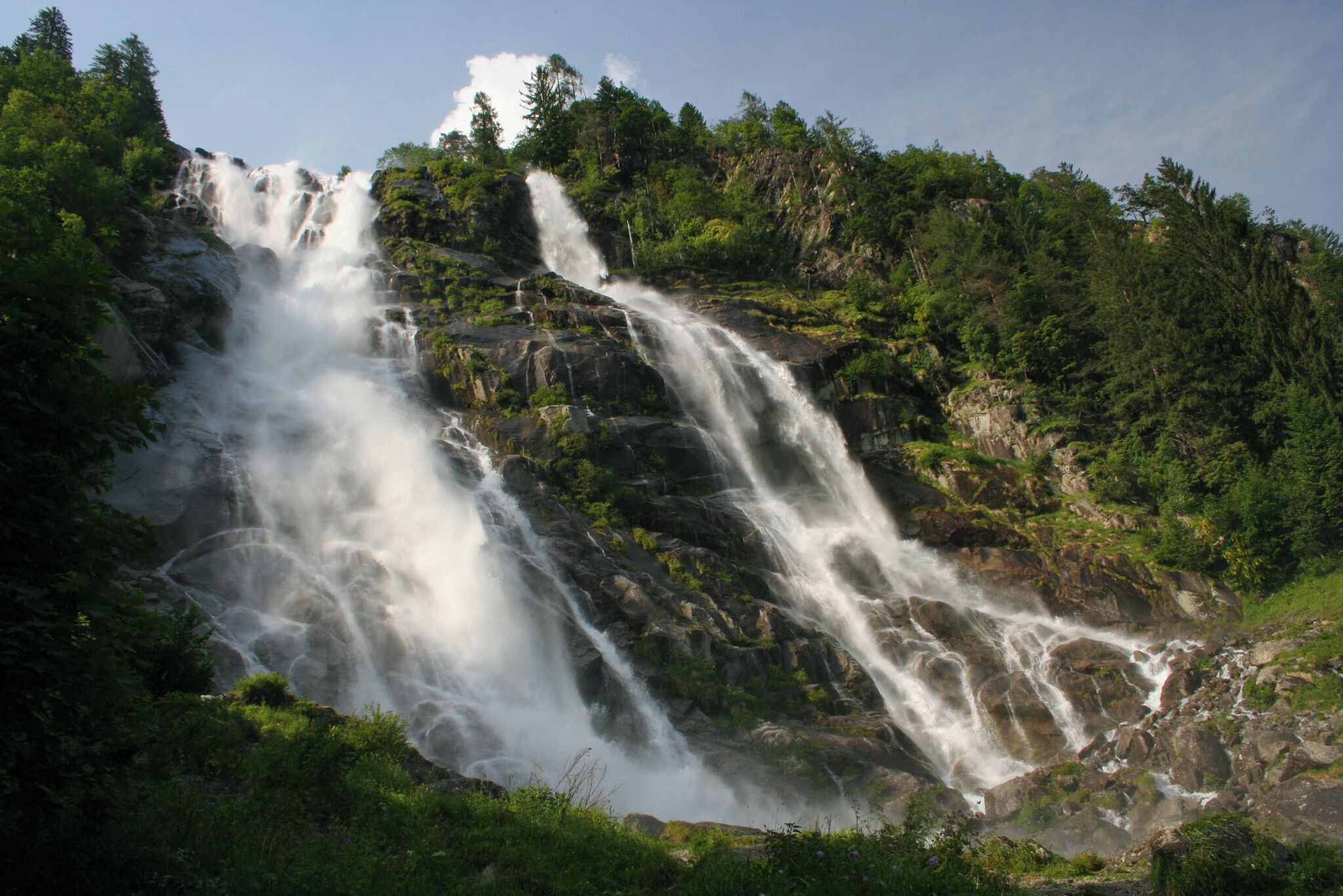 Ein Wasserfall stürzt über felsiges Gelände, umgeben von dichtem Grün.