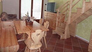 A wooden dining table with chairs, a television on a cabinet, and a wooden staircase. - Studio in the attic with car park (Ponte Arche)