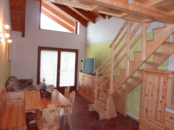 A wooden interior with a dining area, a TV on a cabinet, and a wooden staircase.