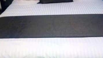 Una cama con ropa de cama blanca y una almohada negra.