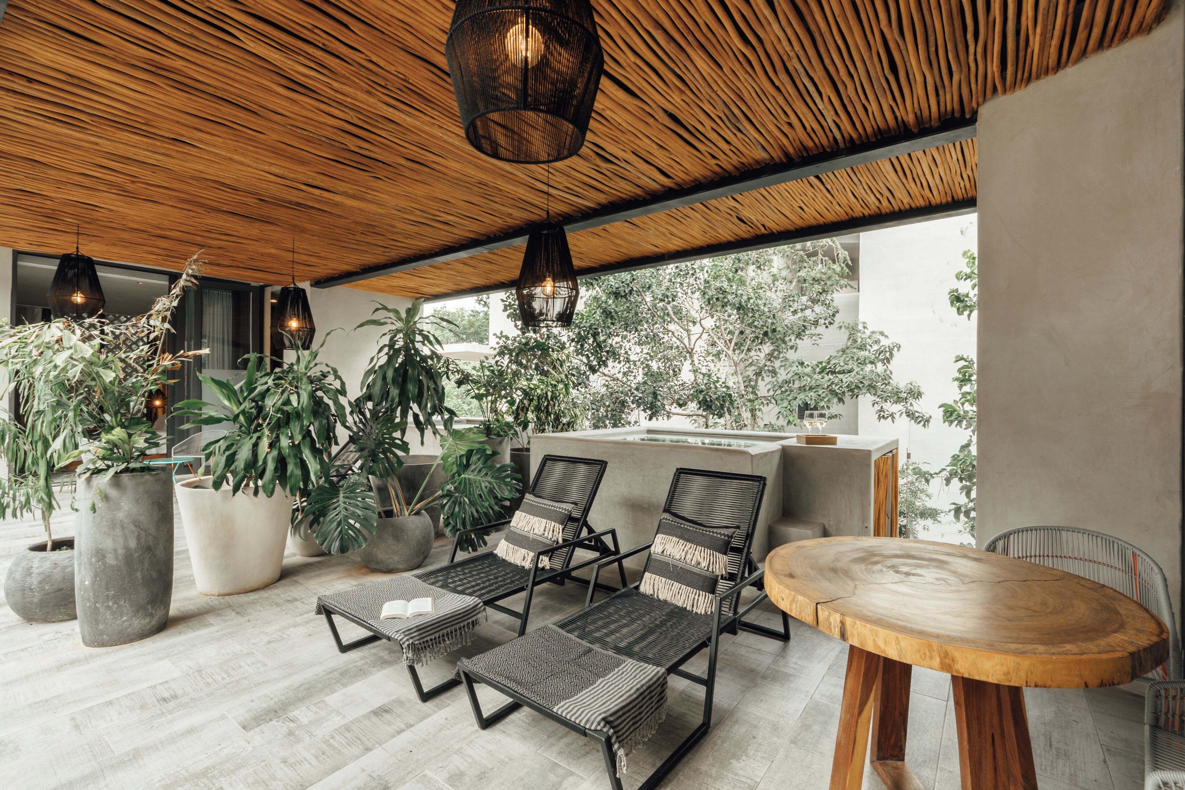 A modern outdoor seating area with lounge chairs, a round wooden table, and large potted plants.