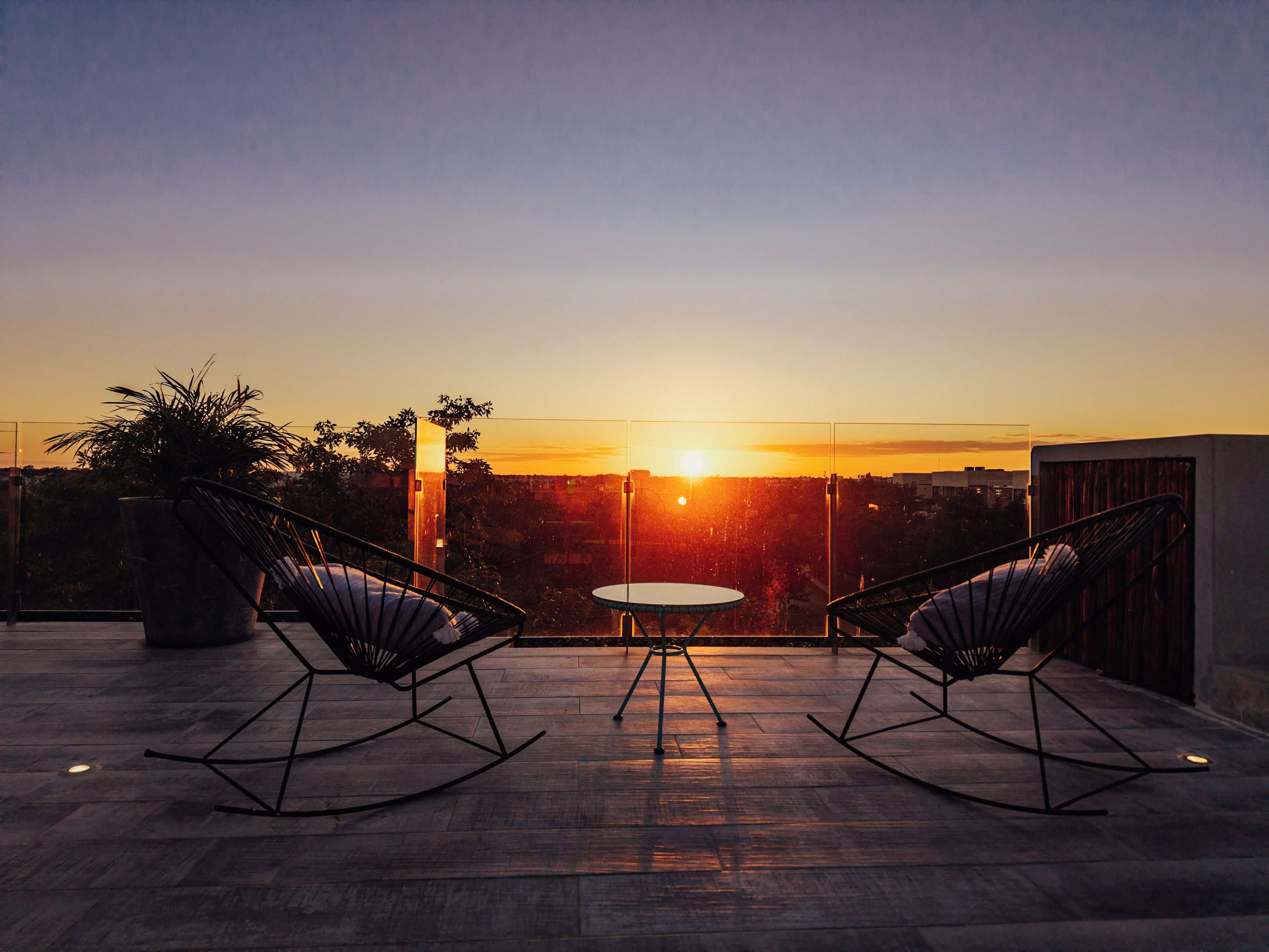 Una terraza con dos mecedoras y una mesa, con vista a un atardecer.
