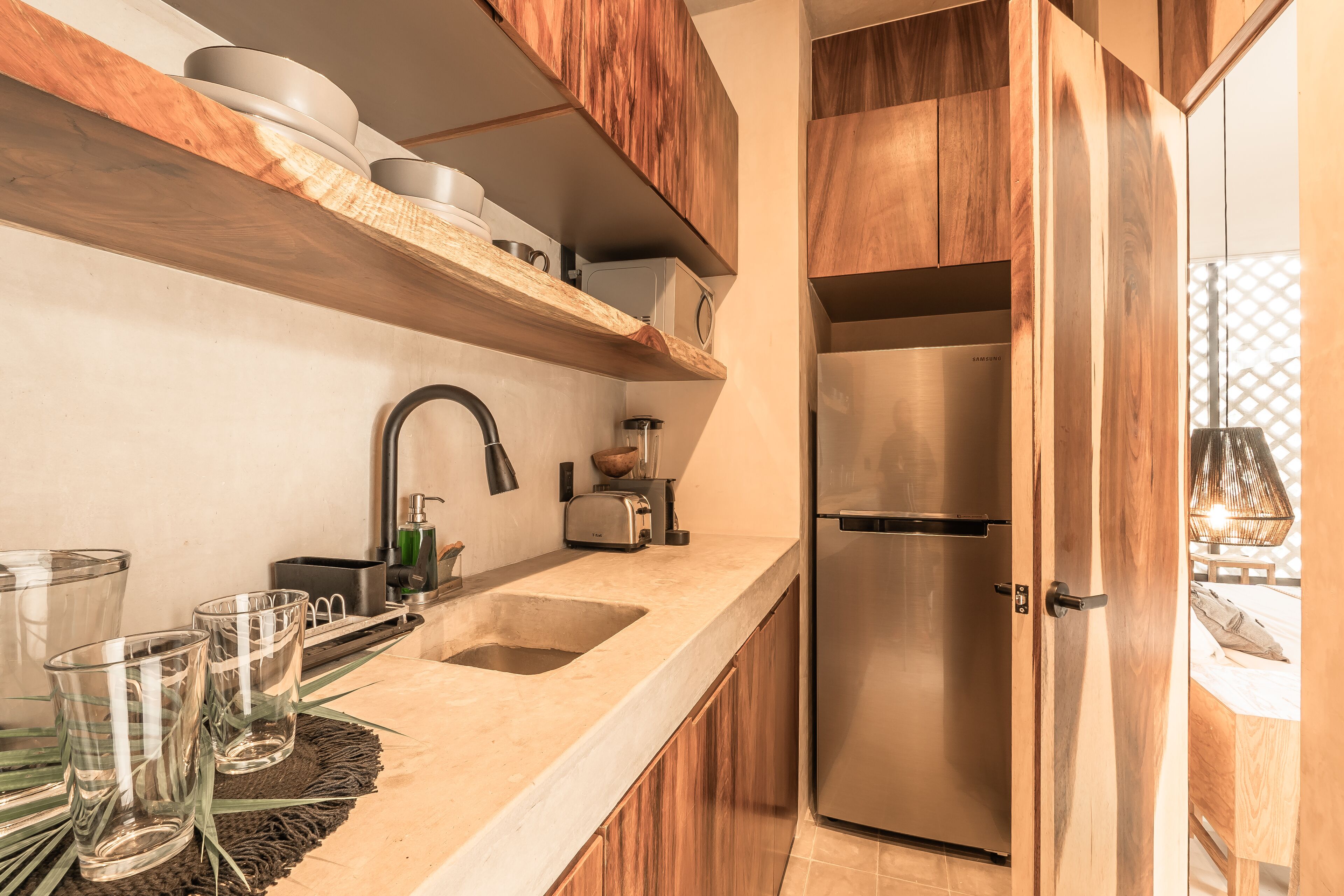 A modern kitchen with wooden cabinets, a stainless steel refrigerator, a double sink, and a countertop with glassware and a toaster.