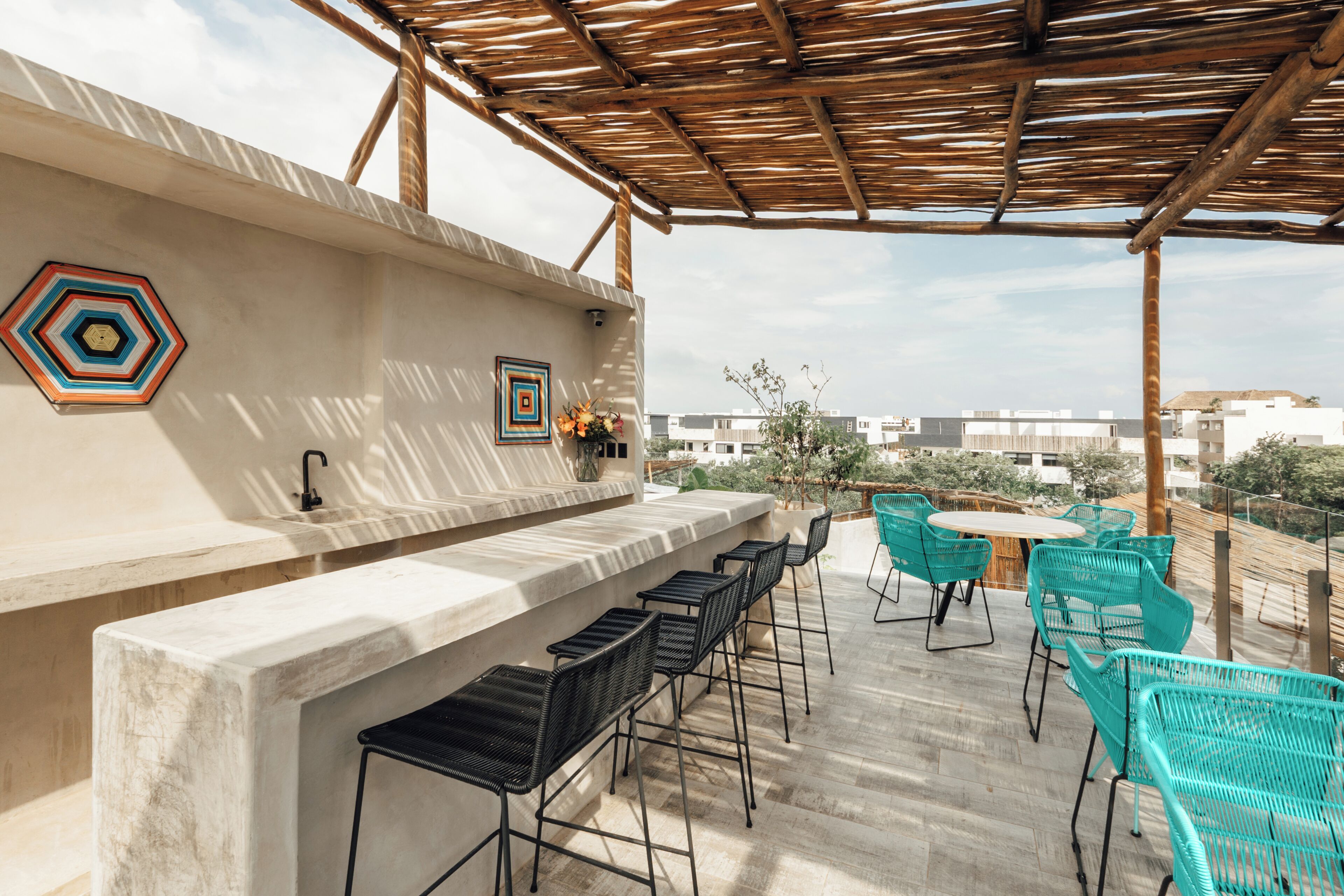 Eine Dachterrasse mit Betonbar, schwarzen Barhocker und türkisfarbenen Stühlen.