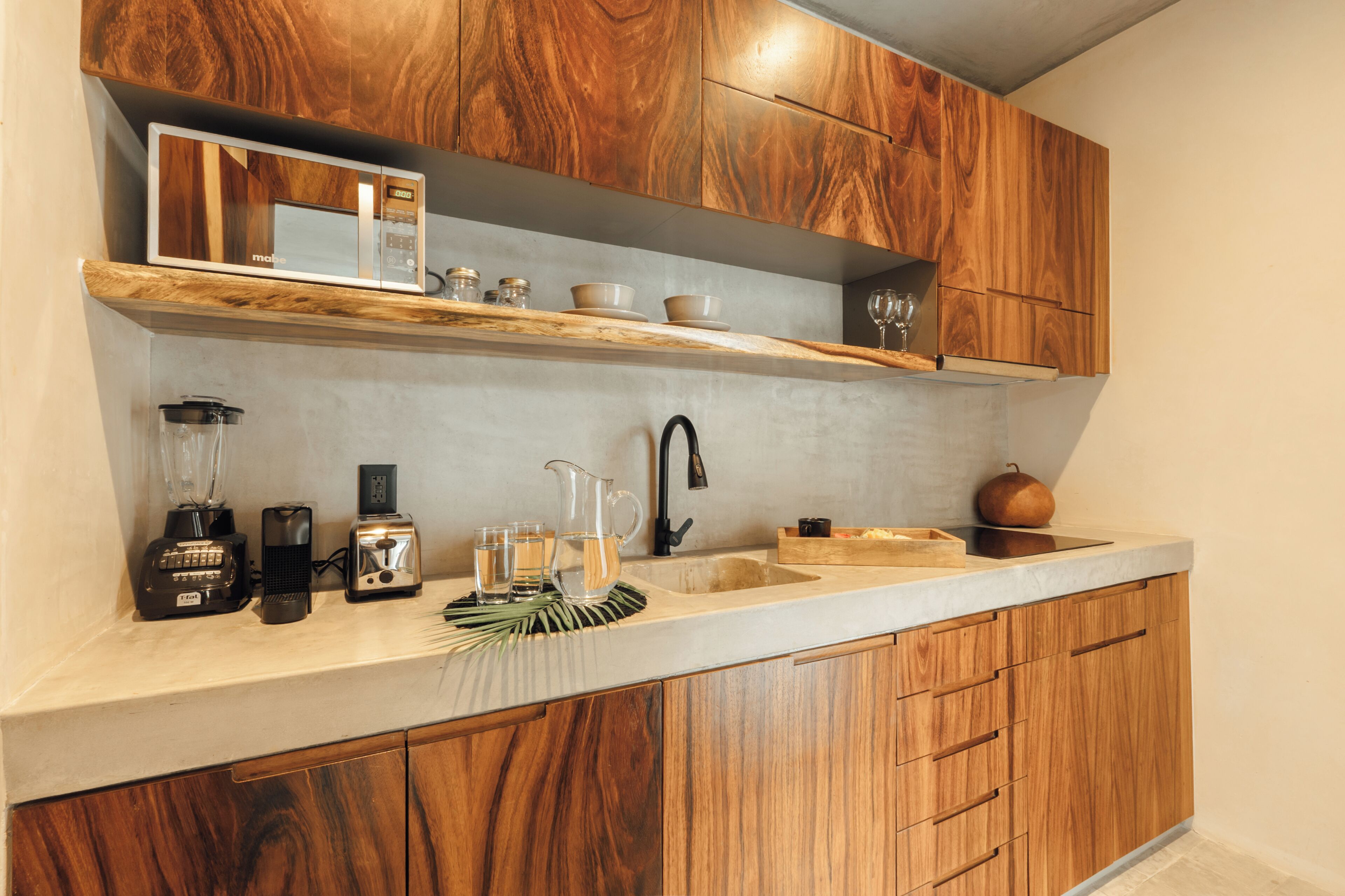 A kitchen with wooden cabinets, a countertop, a sink, a microwave, a blender, a toaster, and a pitcher.