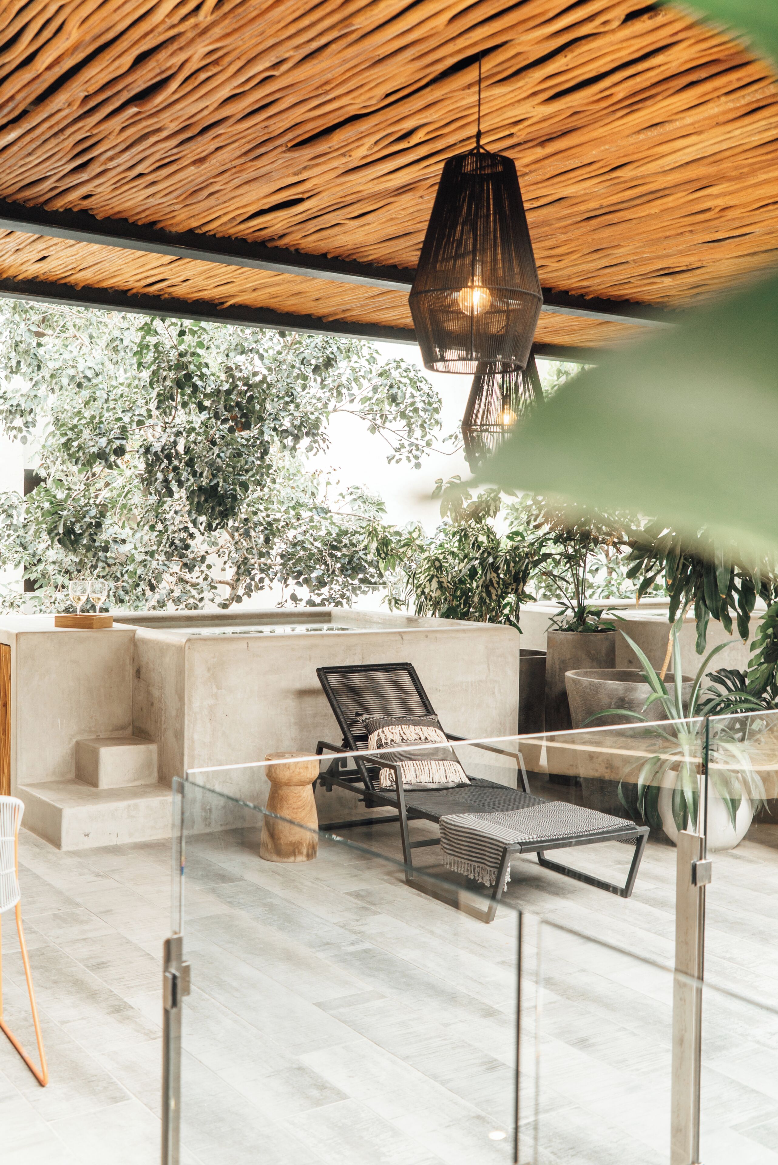 A modern outdoor lounge area with a concrete bench, a lounge chair, and a hanging light fixture.