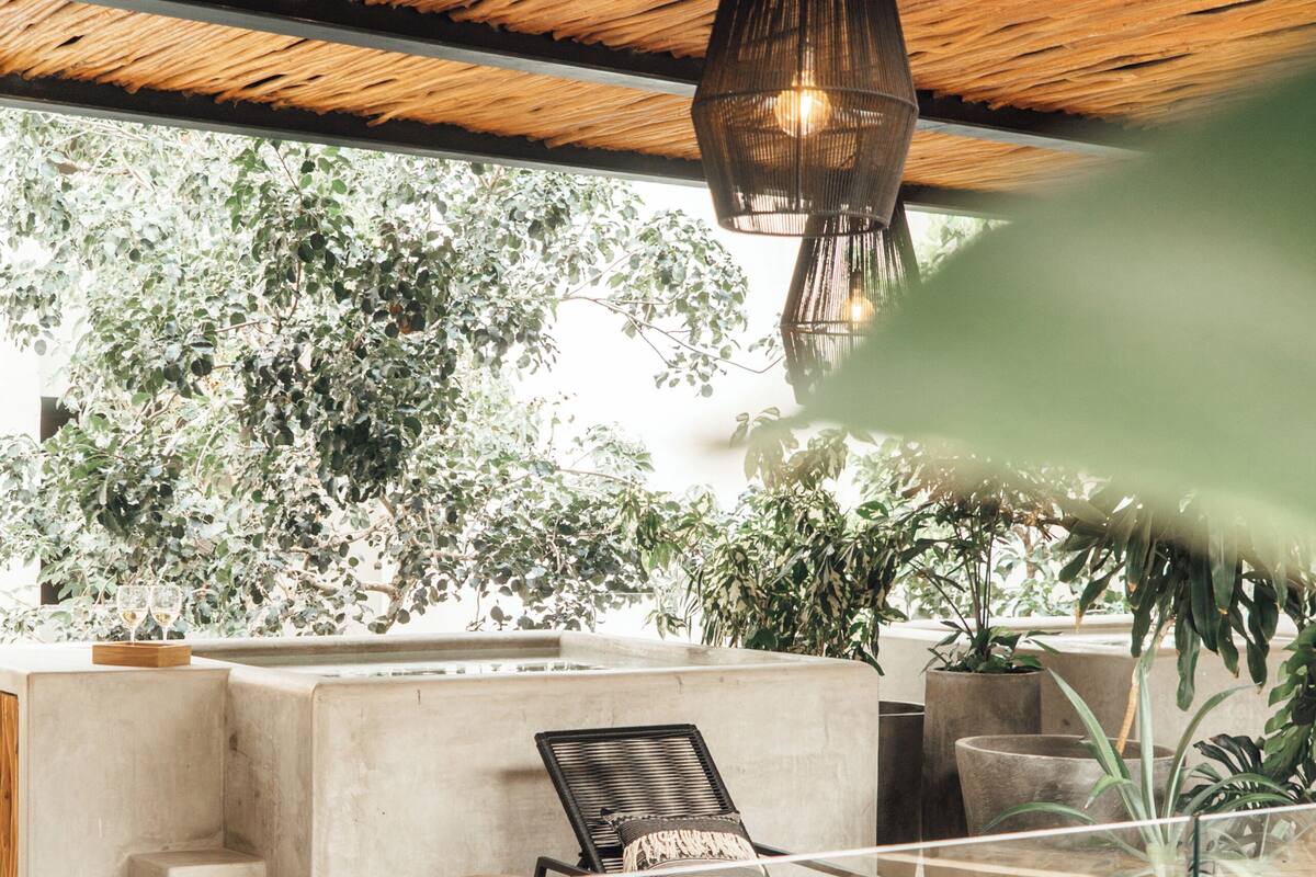 A modern outdoor lounge area with a concrete bench, a lounge chair, and a hanging light fixture.