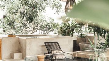 Un espace de détente extérieur moderne, comprenant un banc en béton, un fauteuil et un luminaire suspendu.