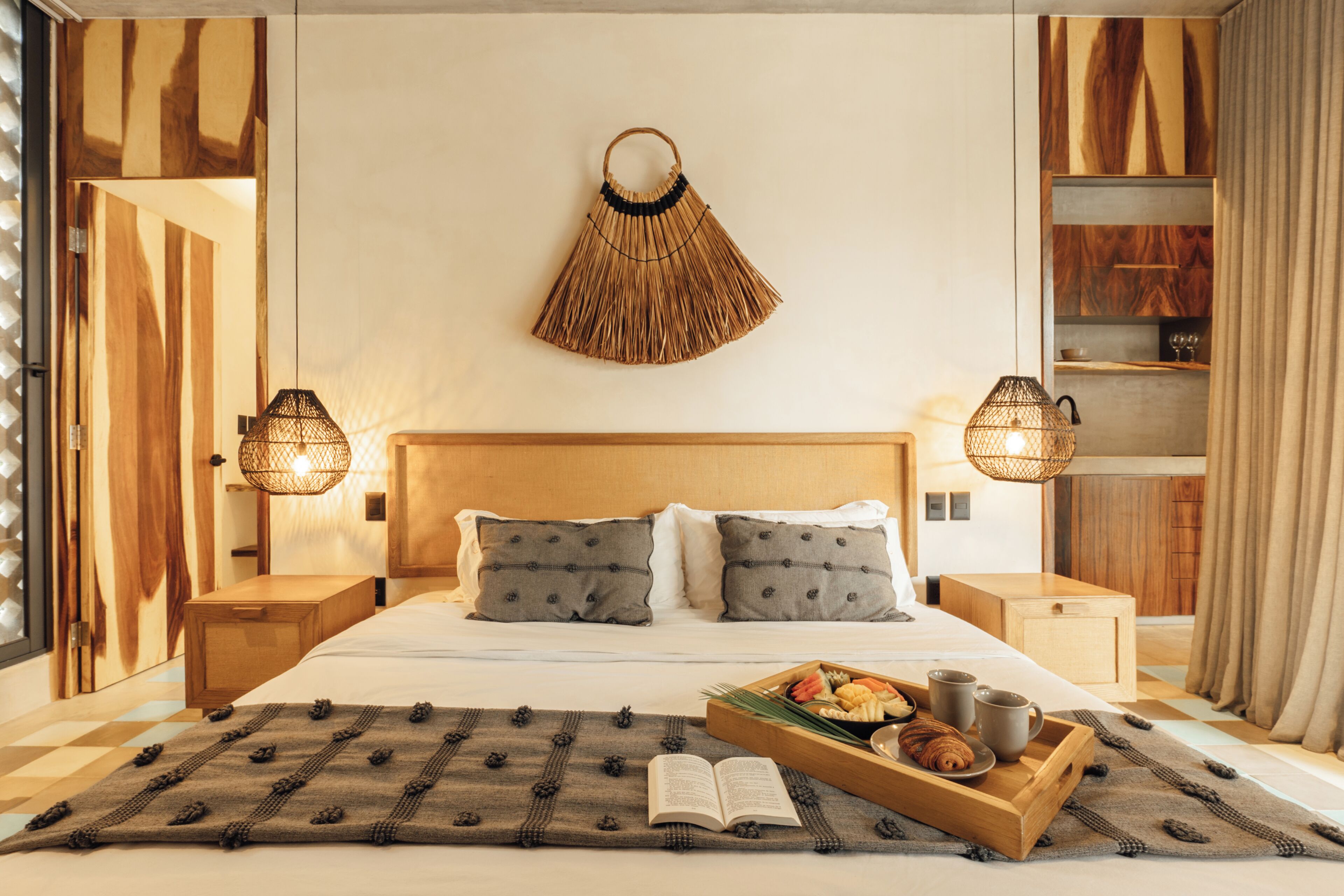 Una camera d'albergo ordinata con un letto, abat-jour, un vassoio con cibo e bevande e un libro sul letto.